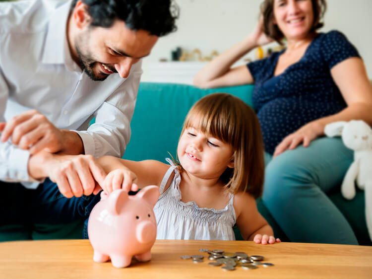 Pregnant mother on sofa with father and daughter looking at piggy bank